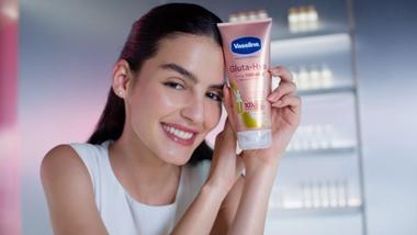 Una donna bianca con capelli scuri e pelle luminosa, con in mano un tubetto di crema Vaseline Gluta Hya Dewy Radiance. Confeziona rosa premium.
