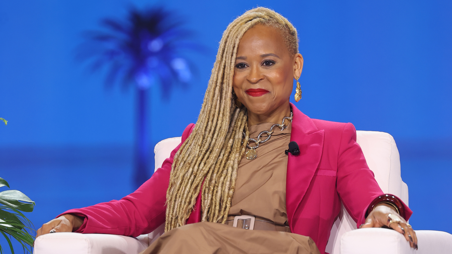 Ritratto di Esi Eggleston Bracey, donna con capelli intrecciati, abito marrone e giacca fucsia.