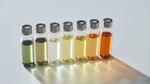 Una fila di sette fiale di vetro con tappi d'argento. Sono riempite con campioni di profumo verde, giallo, ambrato e incolore.