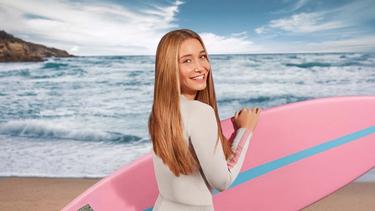 Donna che tiene in mano una tavola da surf sulla spiaggia.