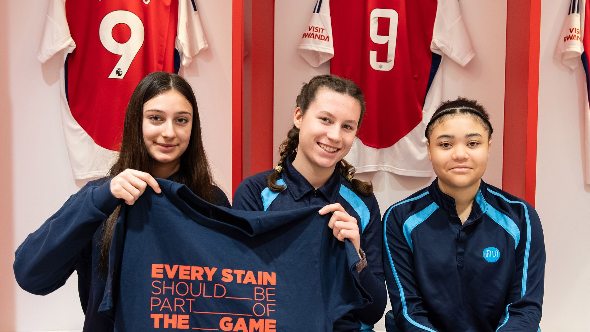 Ragazze nello spogliatoio dell’Arsenal con una maglietta con la scritta “Every stain should be part of the game”, campagna sulla normalizzazione delle macchie nel gioco.