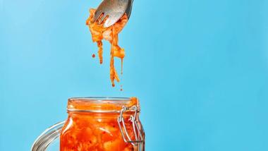 Un getto d'acqua si riversa in un bicchiere d'acqua trasparente pieno di erbe verdi e rosse e fette di barbabietola a strisce bianche e rosse.